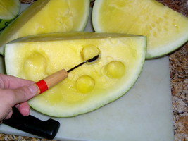 using a melon baller to scoop out bite size yellow watermelon